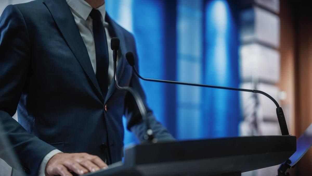 man-stands-podium-with-microphone.jpg