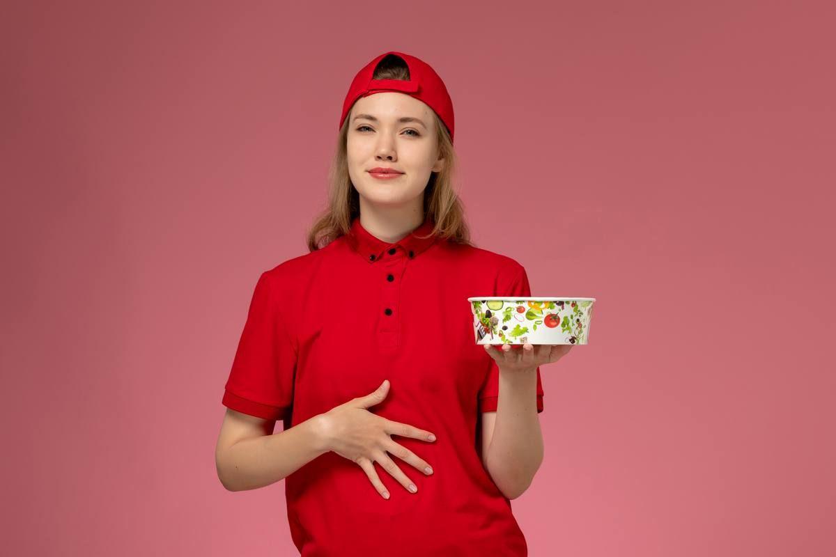 front-view-female-courier-red-uniform-cape-holding-delivery-bowl-light-pink-wall-job-service-uniform-delivery-worker.jpg