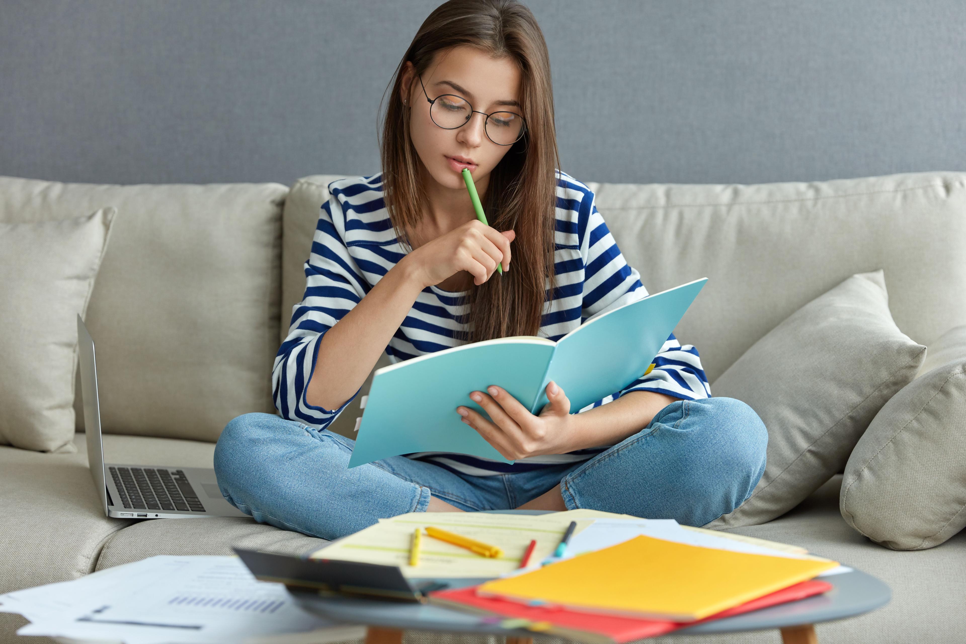 studying-online-concept-serious-young-woman-being-busy-with-remote-freelance-project-sits-comfortable-sofa-writes-notes-holds-textbook-use-laptop-computer-home-with-wireless-internet.jpg