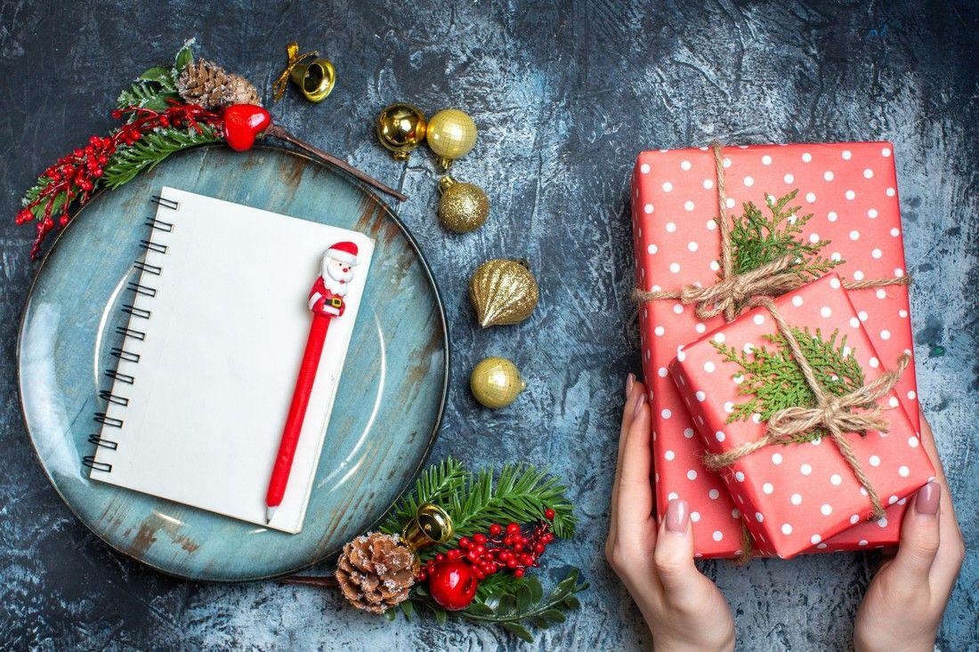 top-view-notebook-with-pen-blue-plate-decorative-accessories-hand-holding-gift-box-dark-background.jpg